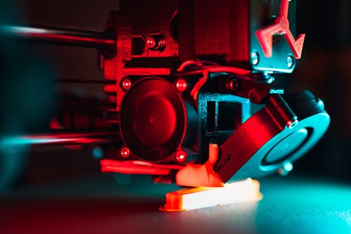3D printer nozzle printing a part under dramatic lighting.
